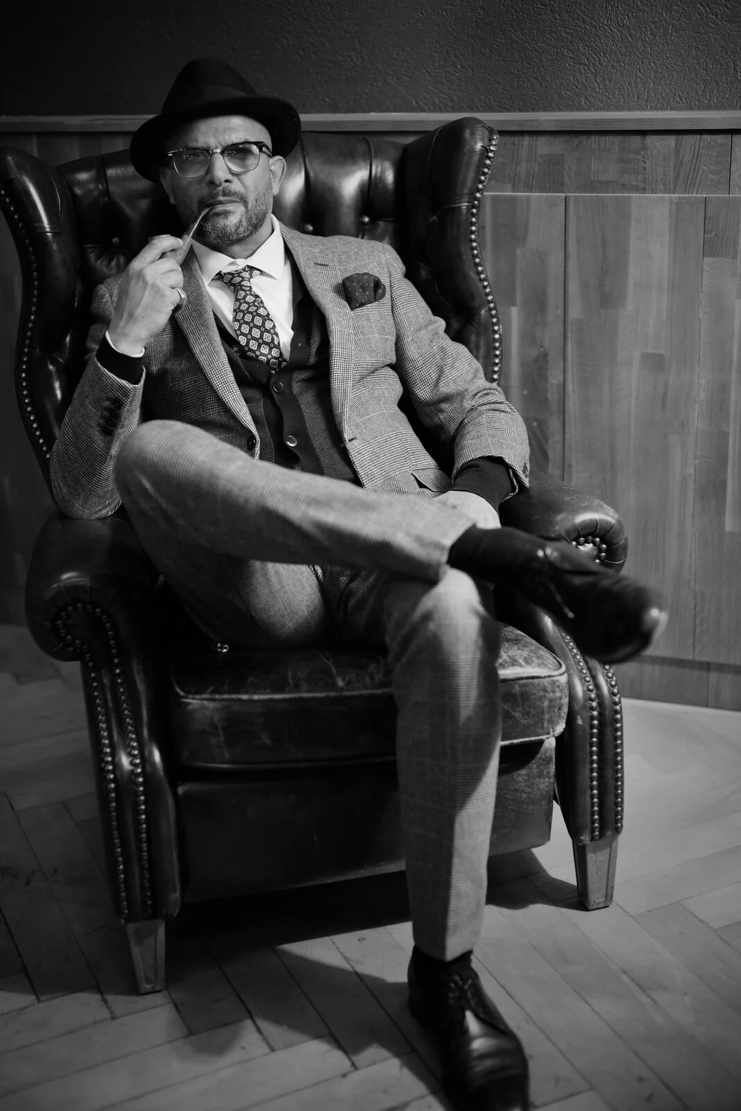 Barber mit Hut, Brille und Anzug im Ledersessel, Schwarz-Weiss – The Barber Zürich